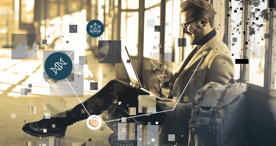 Digitale Selbstbestimmung - lächelnder Mann mit Bart, kurzem Haar und Brille mit Laptop auf dem Schoß und Handy in der rechten Hand, auf dem Boden an eine Wand angelehnt sitzend.