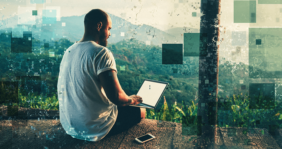 Datensouveränität - Mann mit Bart und Glatze sitzt mit Laptop in der Hand im T-Shirt und mit kurzer Hose mit dem Rücken zur Kamera auf einer Holzterrasse.